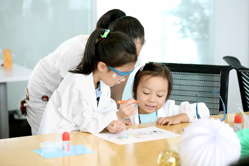 Dvoje dece i žena u belom istraživačkom mantilu boje sliku za stolom