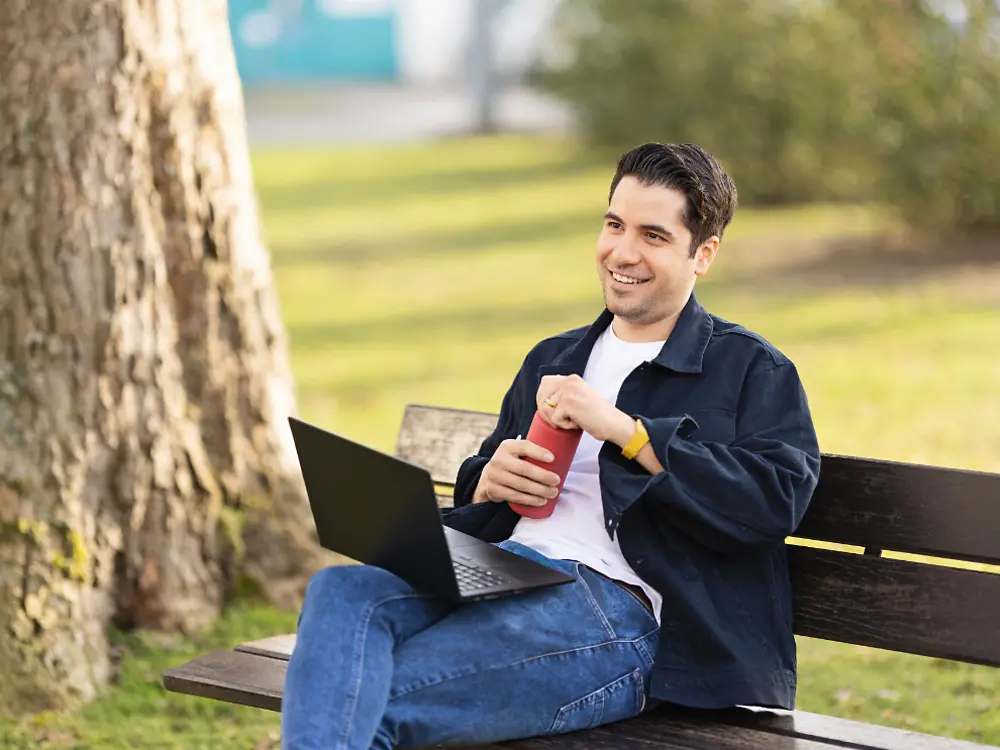 Zaposlenik Henkela sjedi na klupi u parku i radi na svom laptopu.