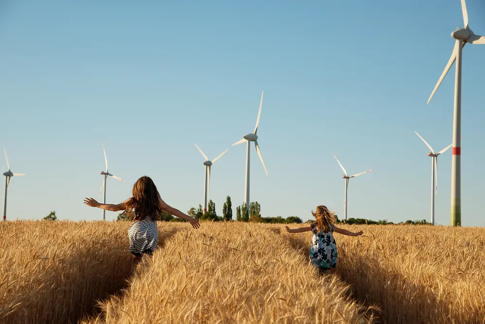 Devojčice trče poljem ka vetrenjačama.
