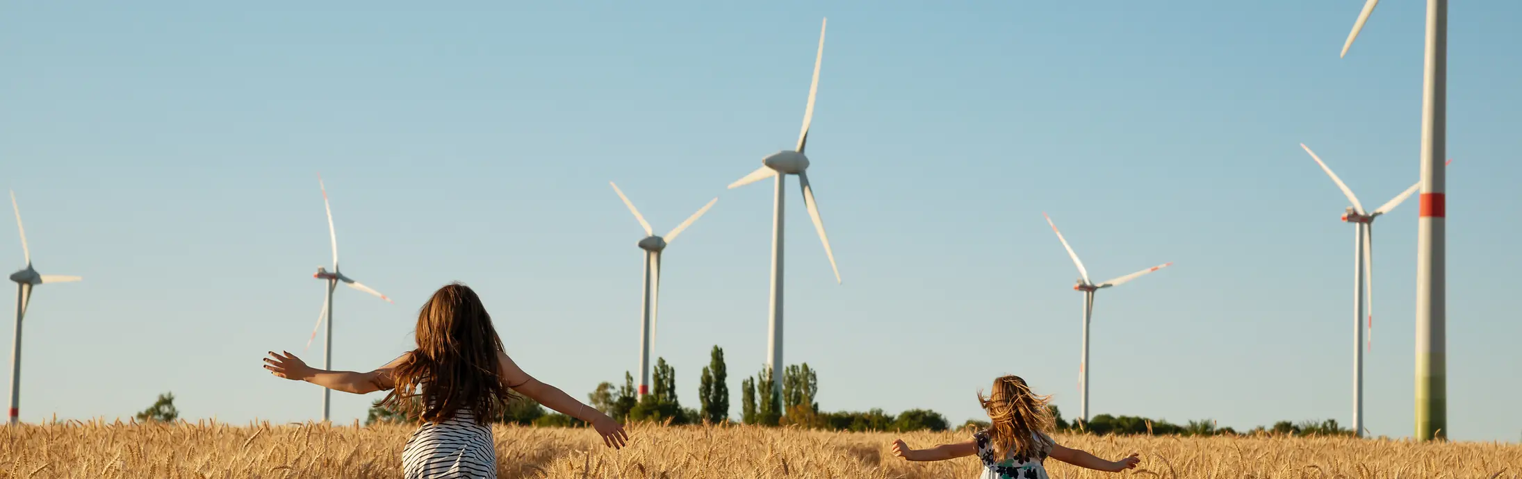 2 girls running in a cornfield with modern windmills in the background