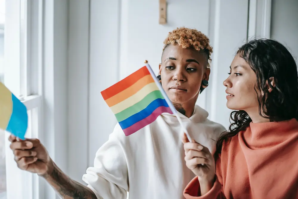 Dve žene razgovaraju dok u rukama drže LGBTQ+ zastave.