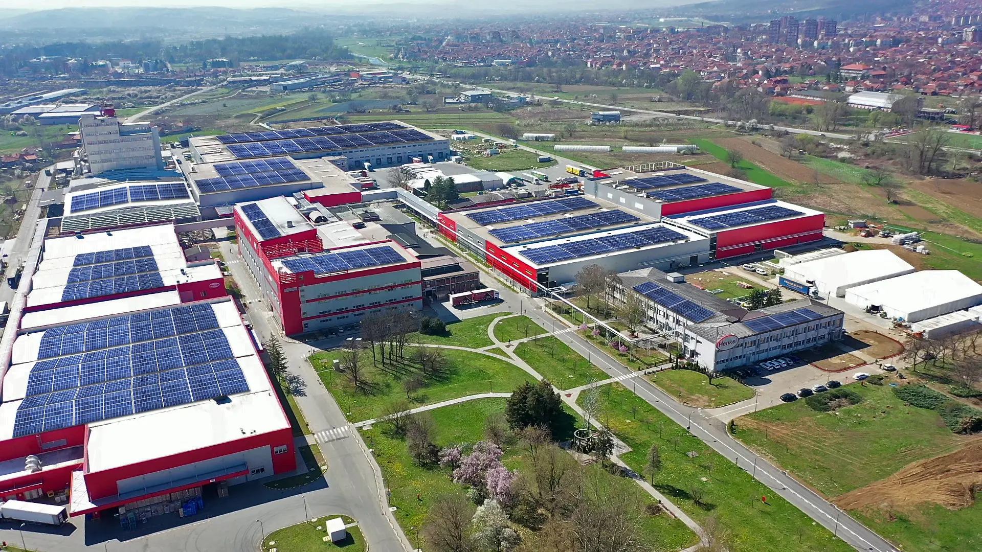 Na fotografiji je prikaz proizvodne lokacije u Kruševcu sa više velikih objekata, crveno-belim fasadama i krovovima prekrivenim solarnim panelima.