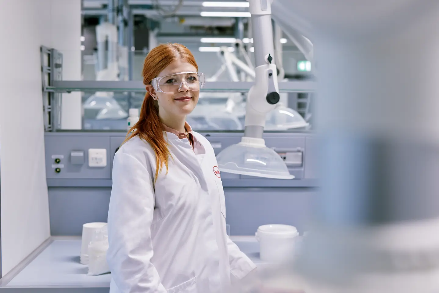 Diplomac koji započinje karijeru u Henkelu, u belom laboratorijskom mantilu, stoji u modernom laboratorijskom okruženju sa tehničkom opremom u pozadini.